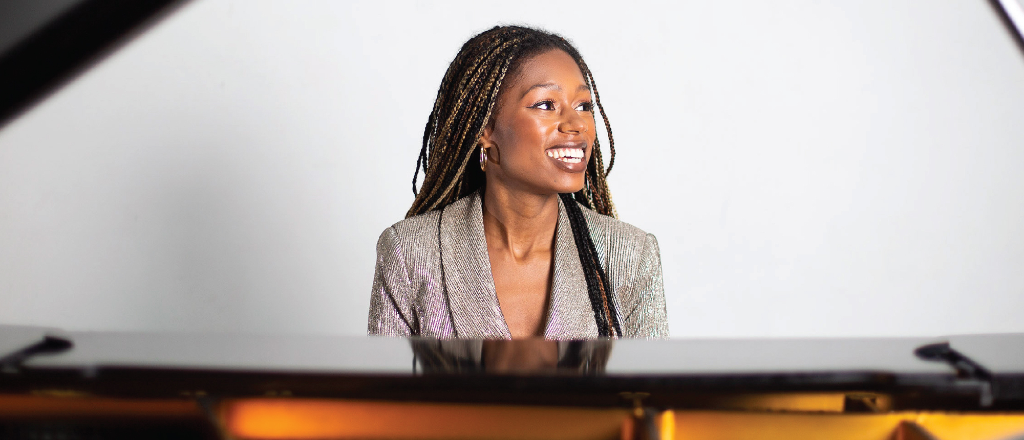 Isata Kanneh-Mason sitting in front of a piano, smiling and looking aside.